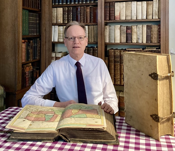 Arie Molendijk zit aan tafel voor een enorm grote oude atlas