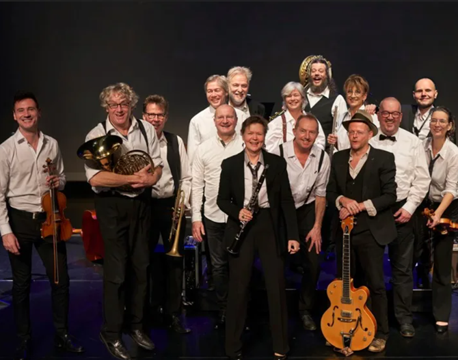 Een grote groep muzikanten op een podium