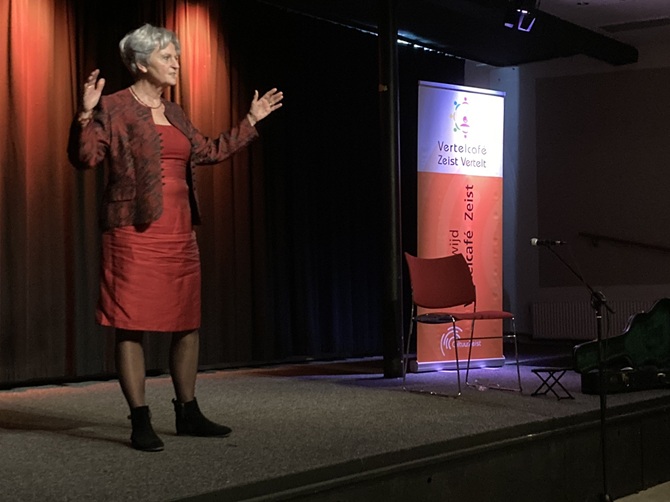 Een verteller vertelt met brede armbewegingen haar verhaal op het podium van het Torenlaan Theater tijdens het Vertelcafé van CultuurZeist