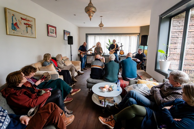 Een gezellige huiskamer vol mensen die luisteren naar een concert tijdens Gluren bij de Buren in Zeist