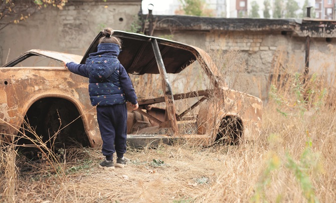 Een kind staat bij een uitgebrande auto in Armenië