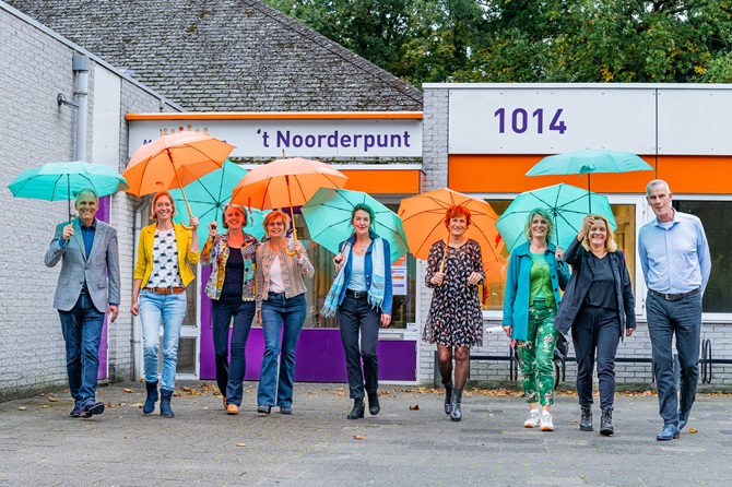 Medewerkers van MeanderOmnium en Samen Oplopen lopen naar de fotograaf toe met ieder een gekleurde paraplu in de hand.