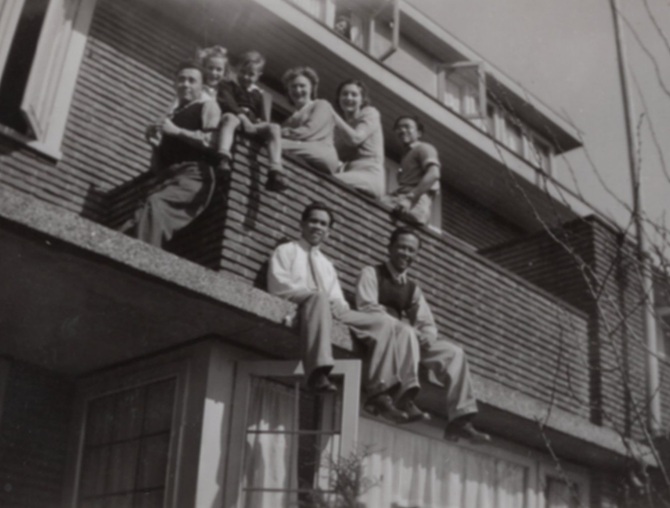 Oude zwartwitfoto waarbij een groep mensen buiten op de rand van een woning zit, ergens in Zeist