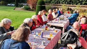 Vrijwilligers zitten aan lange tafels in de Dieptetuin aan een stuk appeltaart