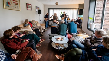 Een gezellig volle huiskamer bij een concert van Gluren bij de Buren in Zeist