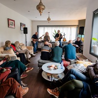 Een huiskamer gezellig vol met buren die luisteren naar een concert van Gluren bij de Buren in Zeist