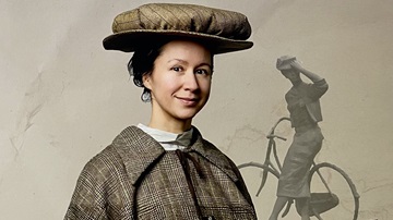 De actrice die Juffer Annie de Beaufort speelt voor het standbeeld van haar op de fiets