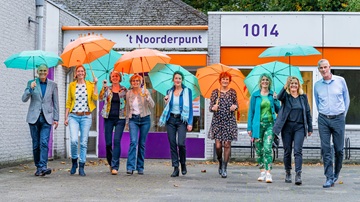 Medewerkers van Samen Oplopen en MeanderOmnium lopen met een groene of oranje paraplu boven zich richting de fotograaf