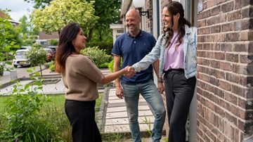 Twee vrouwen schudden elkaar de hand voor de deur van een huis